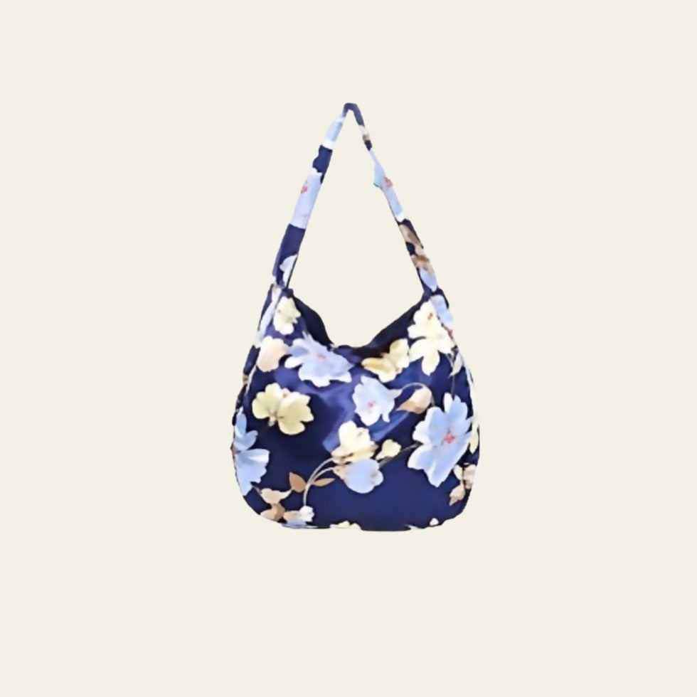 This Boho Bag features a striking floral print with vibrant, colorful flowers that beautifully contrast against the deep blue background of the fabric. Crafted from a silky material, the bag offers a smooth, luxurious feel while maintaining durability and flexibility. Its foldable design adds a practical element, allowing for easy storage and portability.